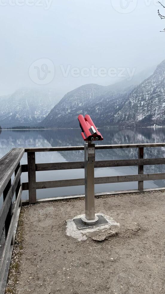 Red Viewing Binoculars Overlooking a Serene Lake Hallstatt and Misty Alpine Mountainous Backdrop photo