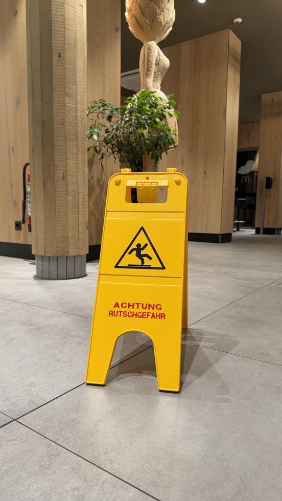 25.03.2025 Germany. Yellow Caution Wet Floor Sign Displayed on Modern Indoor McDonalds Tile Flooring. Detailed close-up view of a warning sign in a stylish modern interior, alerting pedestrians to potential slipping hazards on the tile surface. photo