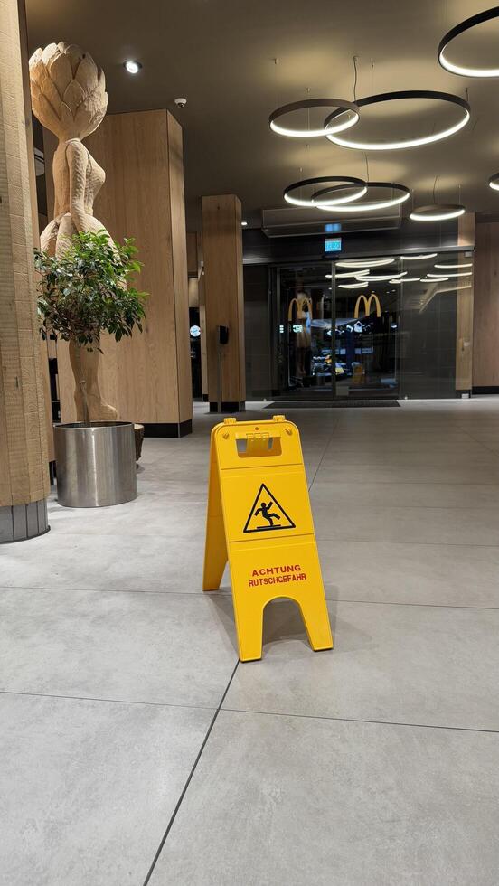 22.03.2025 Germany. Indoor McDonalds Setting Featuring a Caution Sign and Wooden Decorative Art Piece. Modern interior of McDonalds with clean floors, wooden decor, and a bright yellow caution sign emphasizing safety. photo