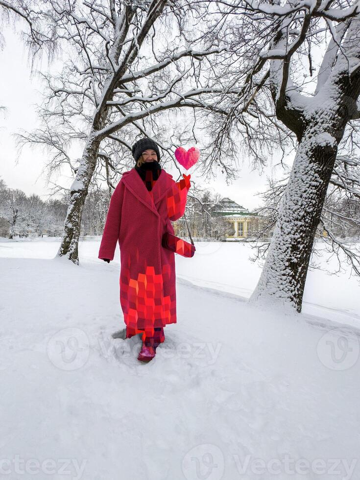 Smiling in a snowy park, a woman in a pink geometric-patterned coat and matching boots has a pixelated heart hovering above her hand. photo