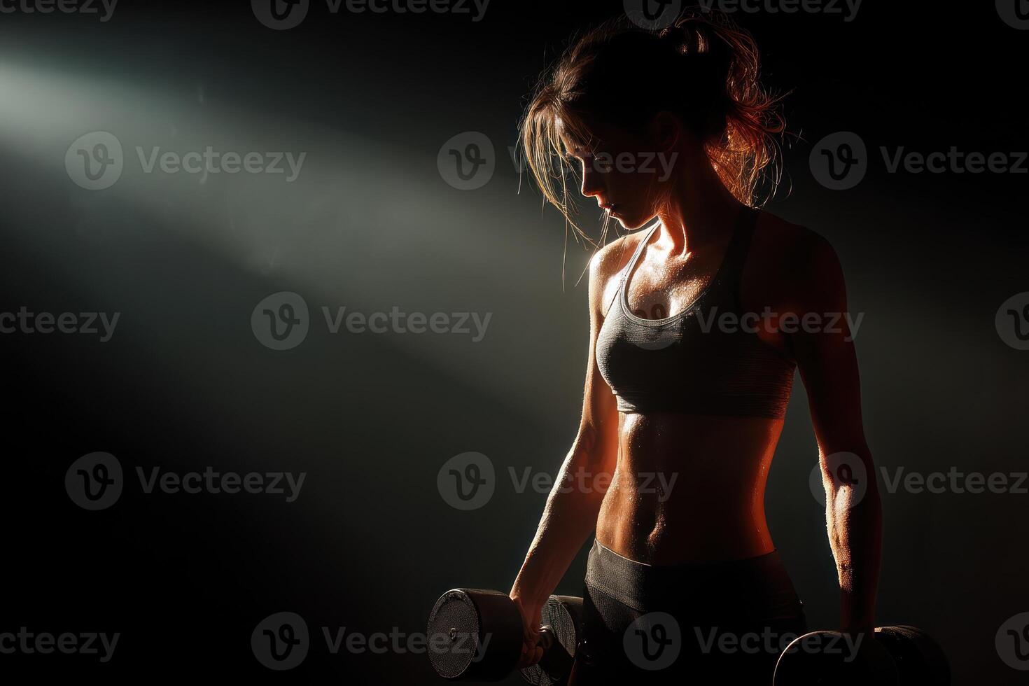 determined woman lifting dumbbells in dark gym, showcasing strength and fitness under dramatic lighting photo
