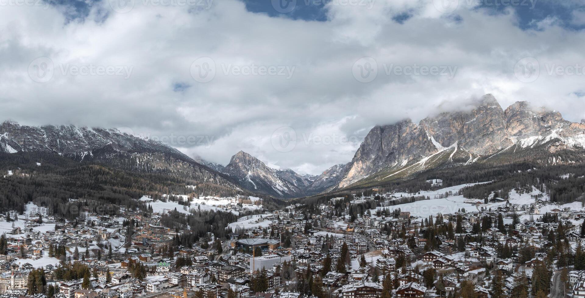 Aerial view of Cortina d'Ampezzo in Italy, featuring snow dusted rooftops, alpine buildings, dense forests, and the Dolomites with Olympic preparations. photo