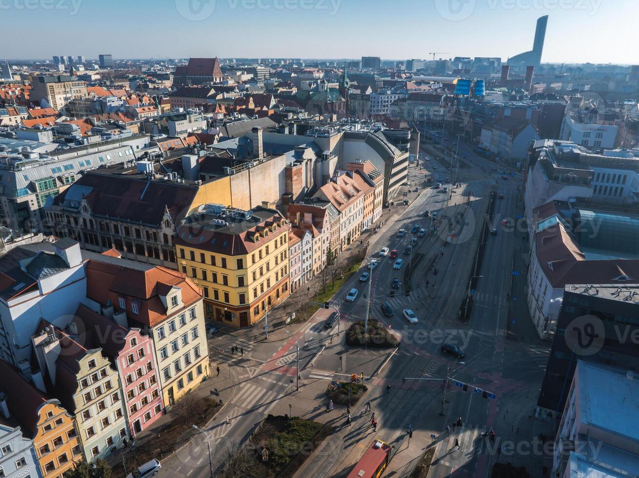Aerial image of Wroclaw, Poland, showing colorful gabled townhouses, modern buildings, a tall structure, tram tracks, and a busy intersection. photo