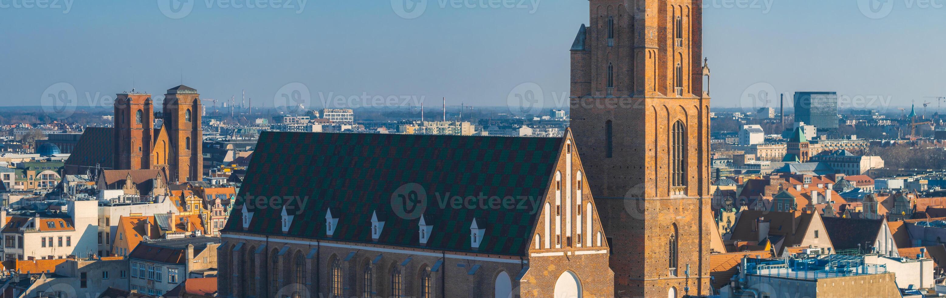 Aerial view of Wroclaw, Poland, showcasing a Gothic style church with a tall brick tower, colorful tiled roof, and a mix of historic and modern buildings. photo