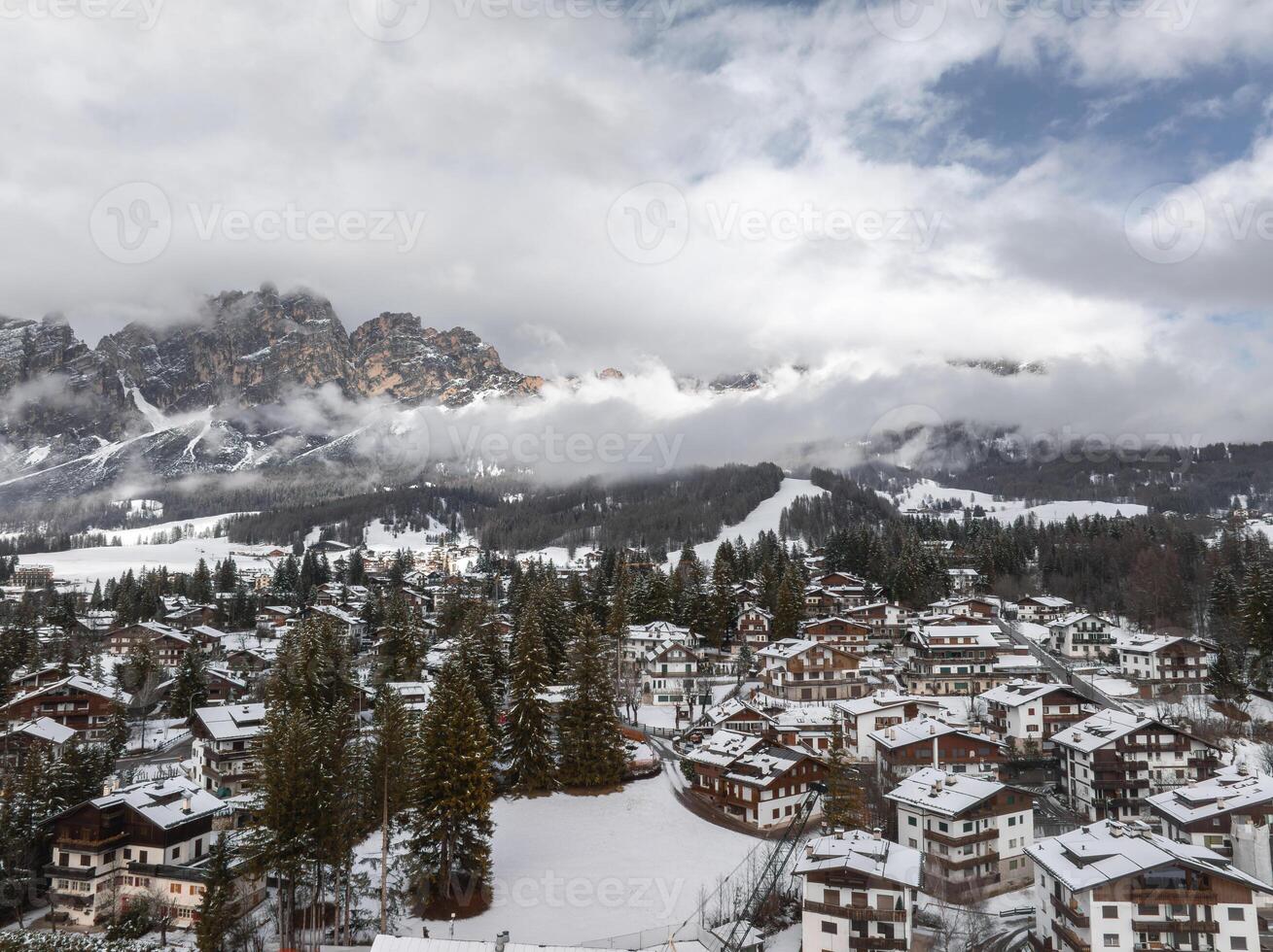 Aerial view of Cortina d'Ampezzo in Italy, featuring snow covered rooftops, evergreen trees, ski slopes, and the dramatic peaks of the Dolomites. photo