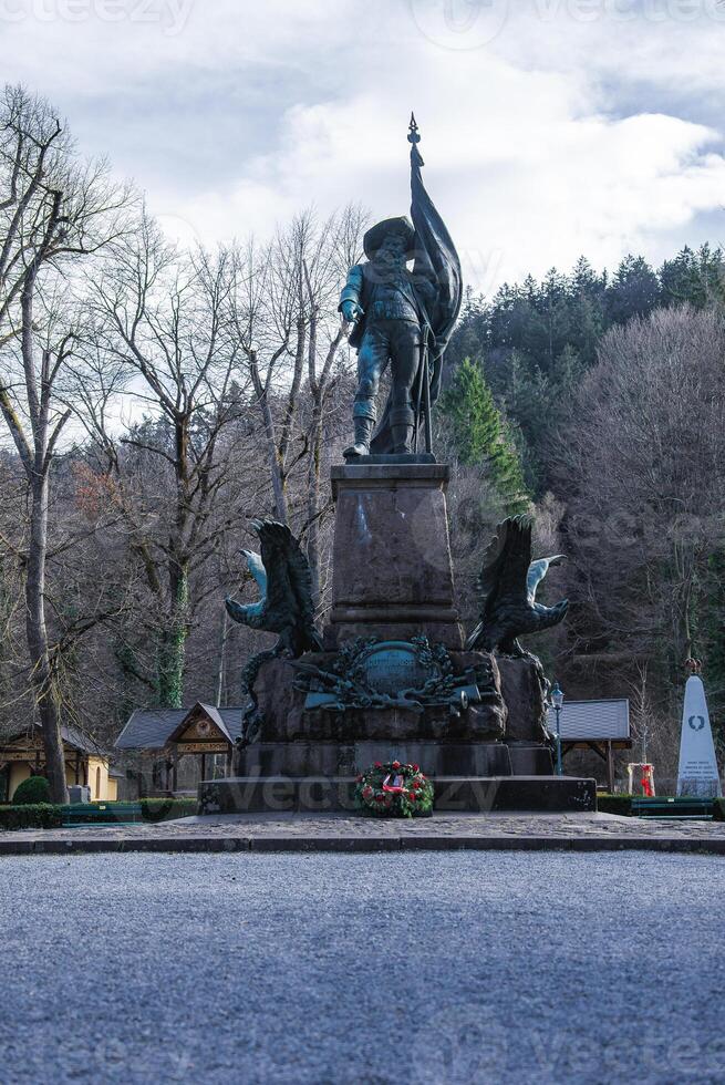 A statue of a historical figure holding a flag stands on a detailed pedestal with sculpted eagles, surrounded by leafless trees and memorial elements in Innsbruck, Austria photo