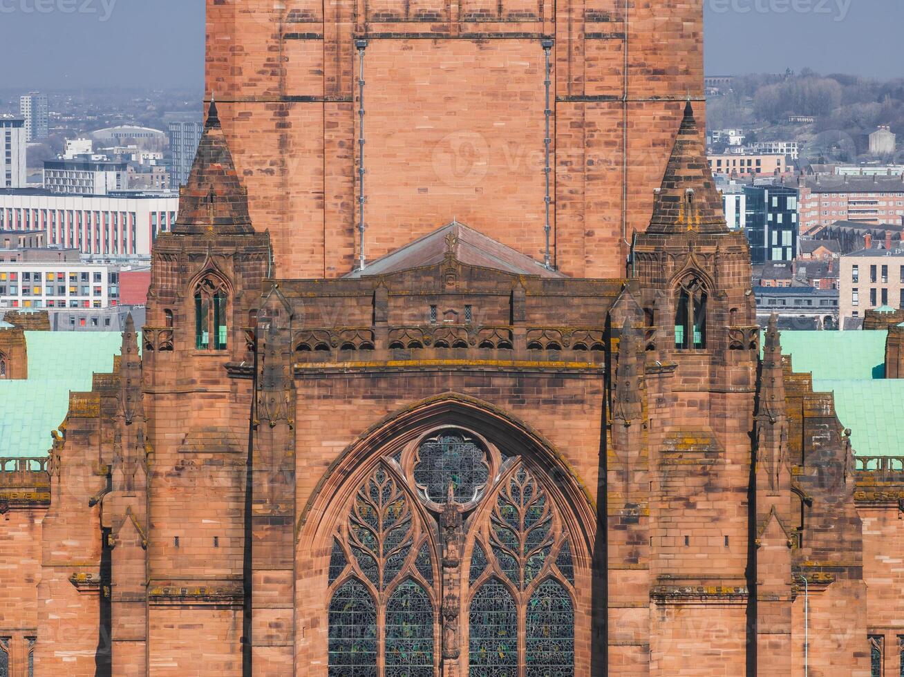 Liverpool Cathedral's Gothic architecture with red sandstone, copper roof, and stained glass window, set against modern urban buildings in Liverpool, England. photo