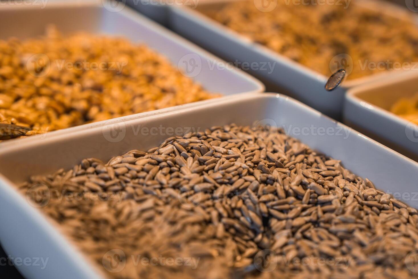 White trays filled with sunflower seeds and grains are neatly arranged under warm lighting, part of a breakfast buffet in the Italian Alps. photo