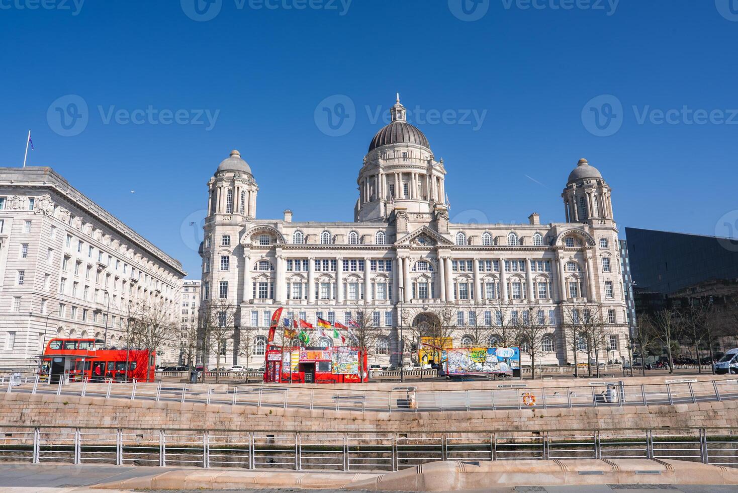 The Port of Liverpool Building in England features Edwardian Baroque architecture, colorful art installations, red double decker buses, and a clear blue sky. photo