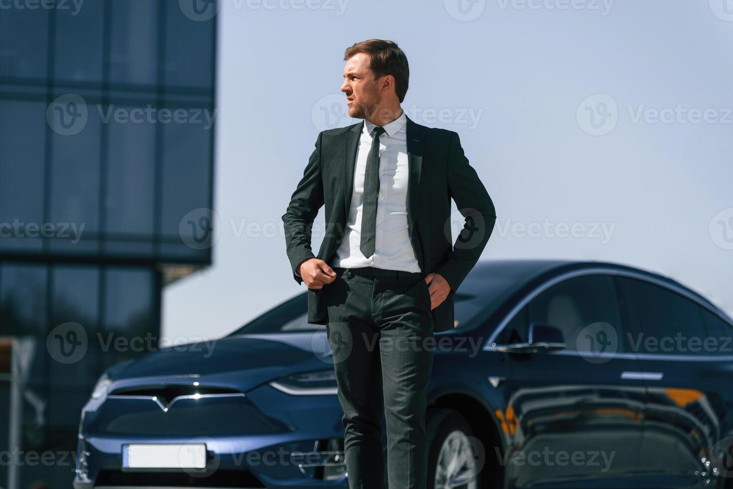 Business building behind. Man in suit and tie is standing near his ,car ,outdoors photo