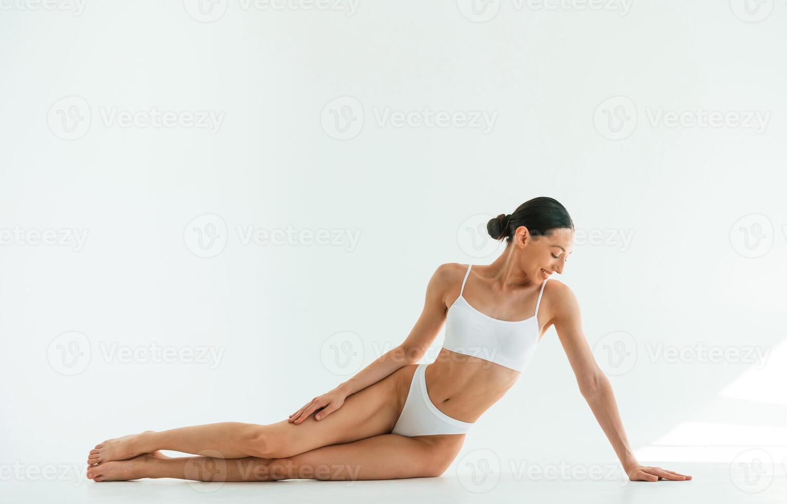 Taking a break, sitting, on the floor. Young woman with slim body type is in fitness clothes in the studio photo