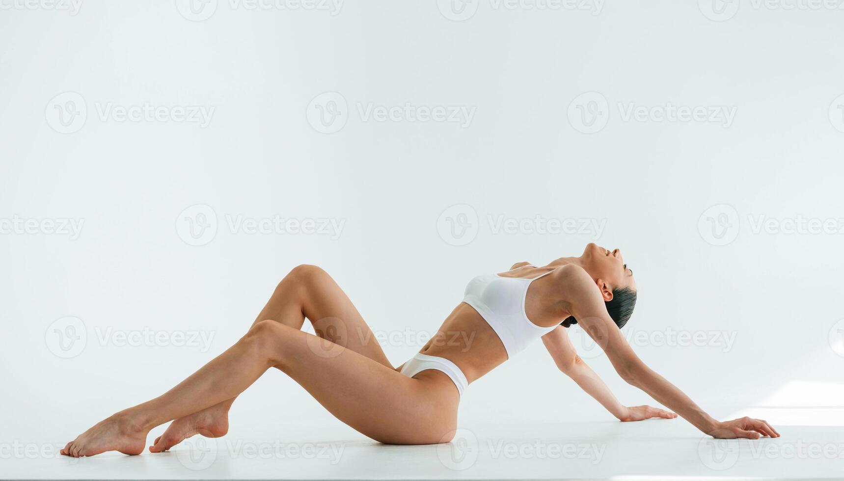 View from the side, on the floor... Young woman with slim body type is in fitness clothes in the studio photo