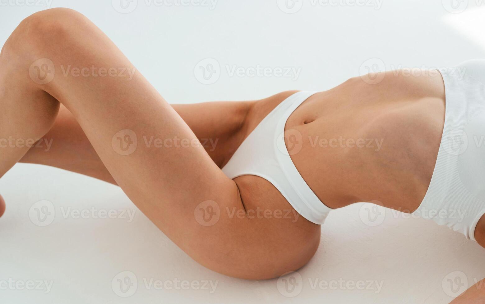 Close up, view, of belly, on the floor. Young woman with slim body type is in fitness clothes in the studio photo