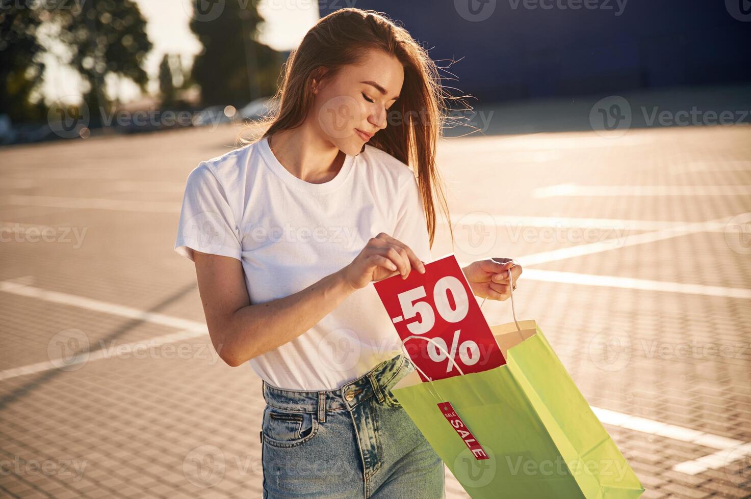 Minus fifty, percent sale. Half the price. Beautiful woman in casual clothes is holding shopping bags, outdoors photo