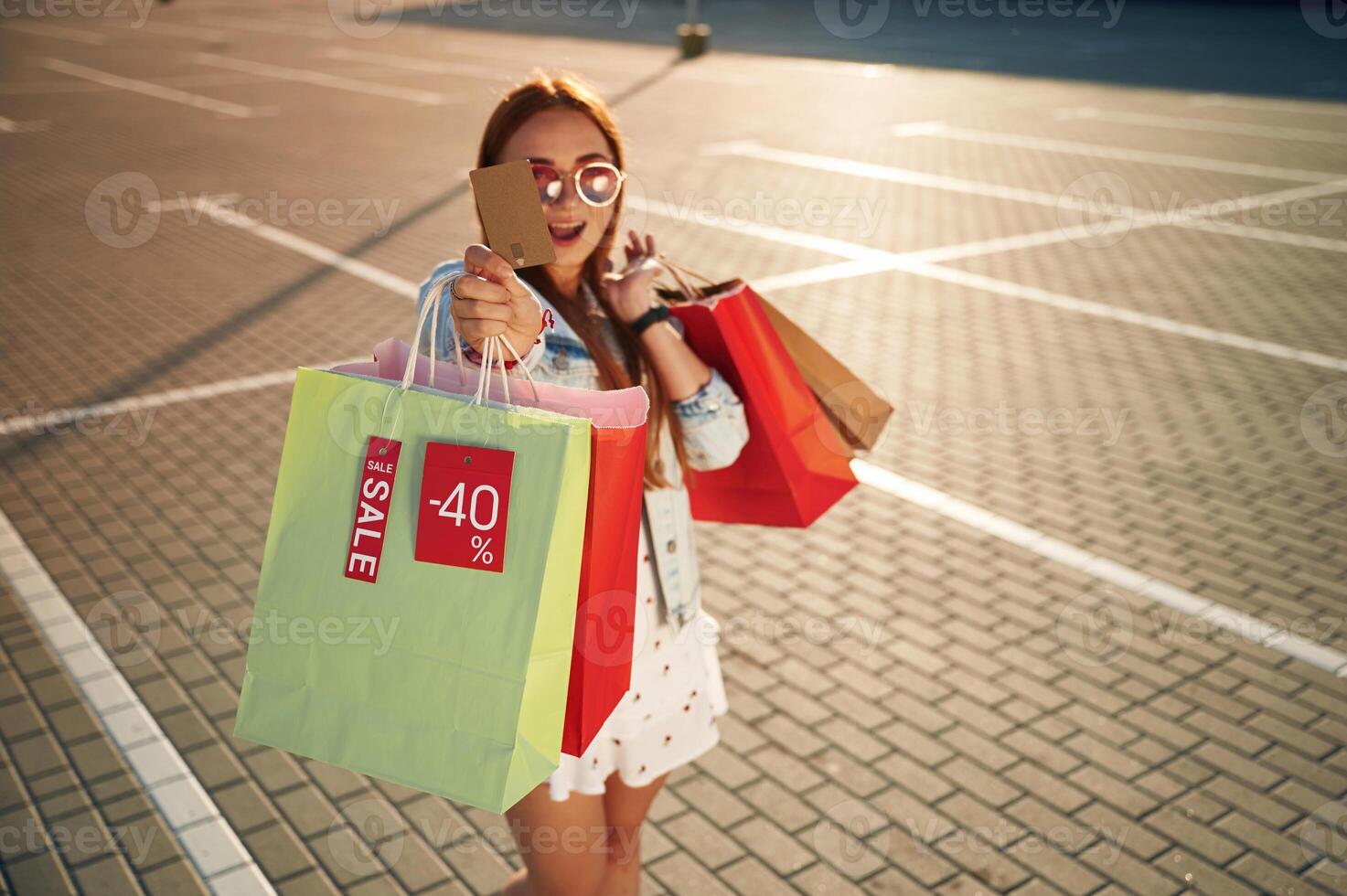 Discounts, with credit card ,in, hands. Beautiful woman in casual clothes is holding shopping bags, outdoors photo