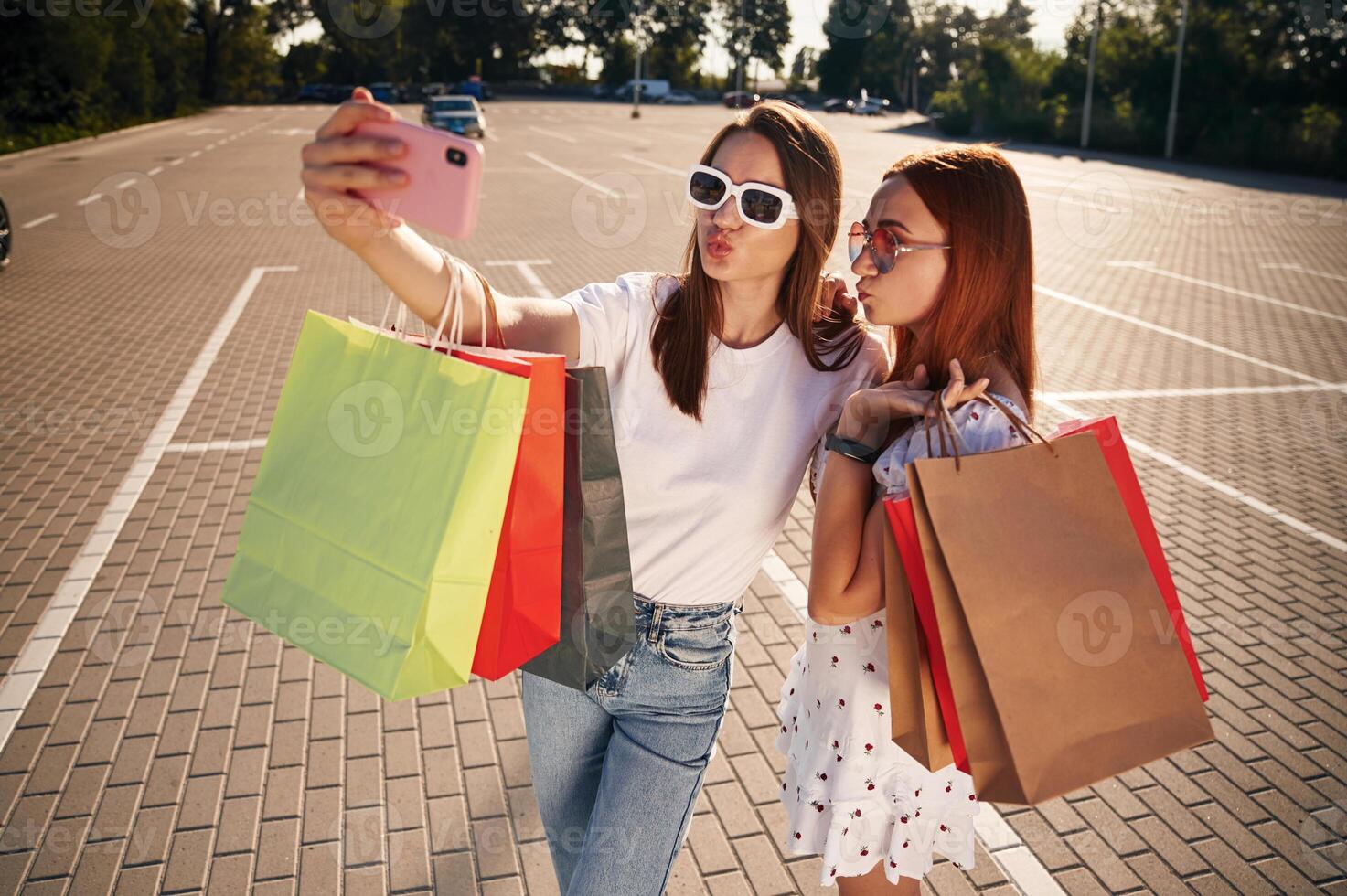 Taking ,a selfie. Two beautiful women in casual clothes are holding shopping bags, outdoors photo