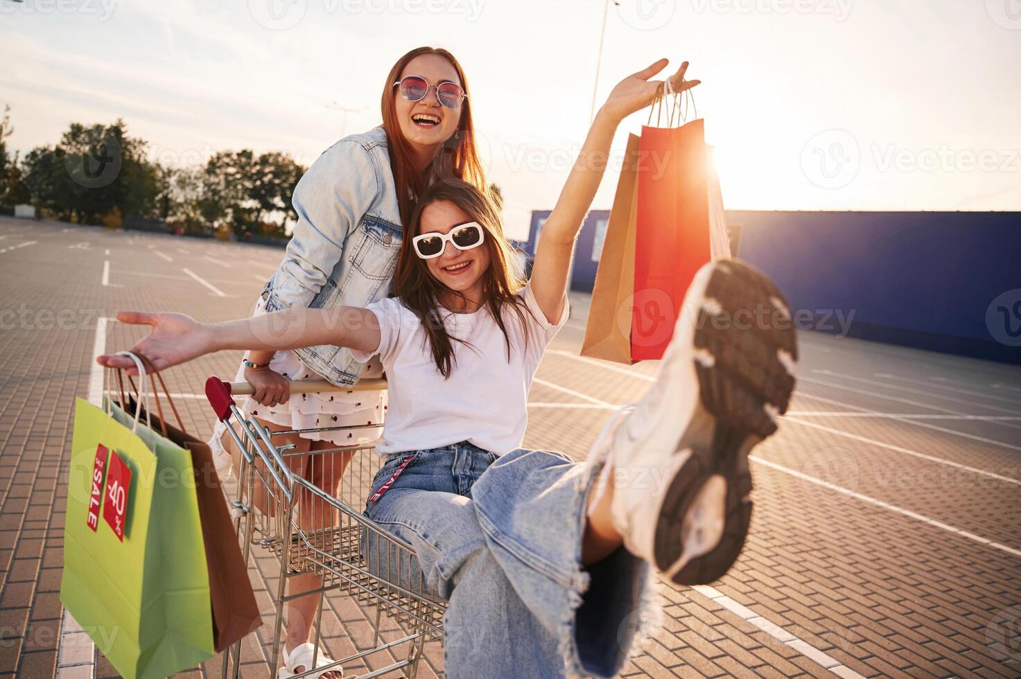 Friends are enjoying riding ,on shop ,cart. Two beautiful women in casual clothes are holding bags, outdoors photo