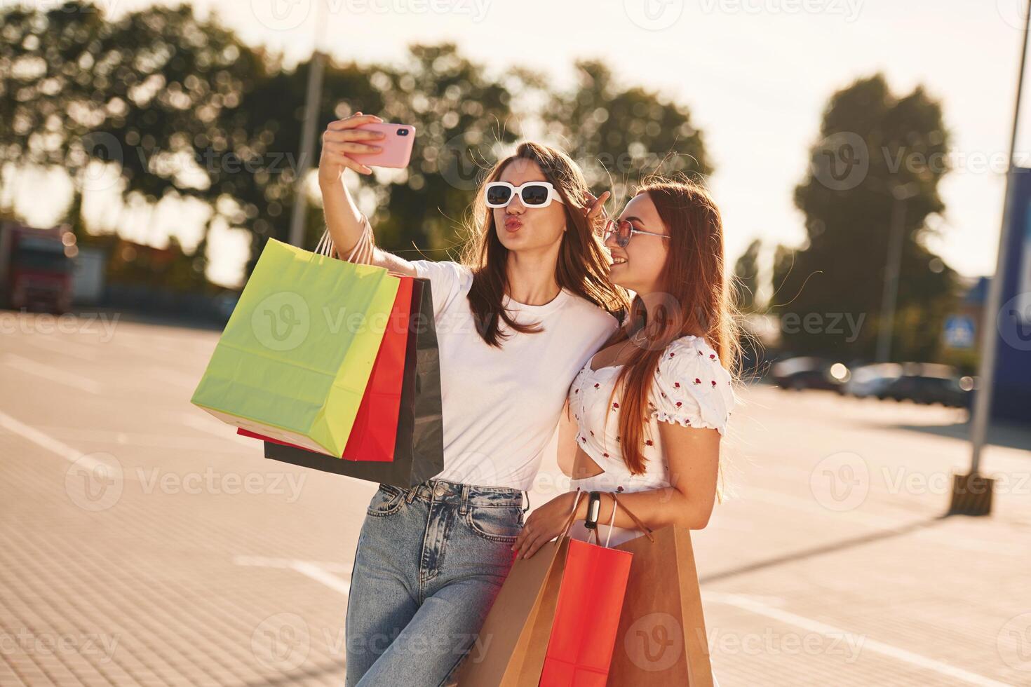 Two beautiful, women in casual clothes, are holding shopping bags, outdoors photo
