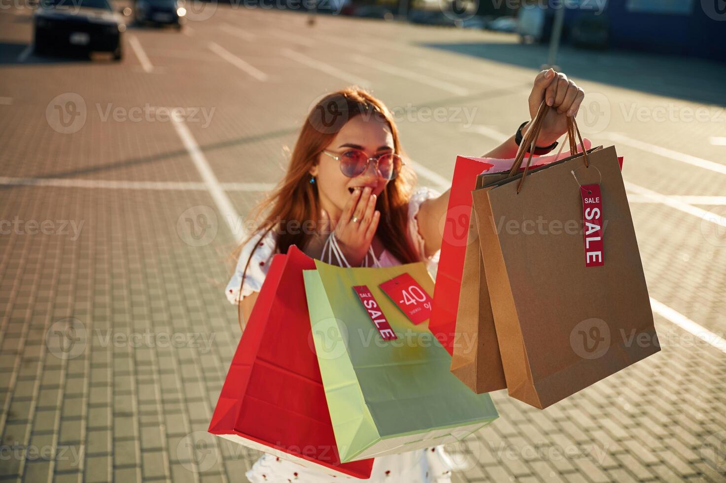 Showing shopping bag, with sale stickers on it. Beautiful woman in casual clothes is outdoors photo