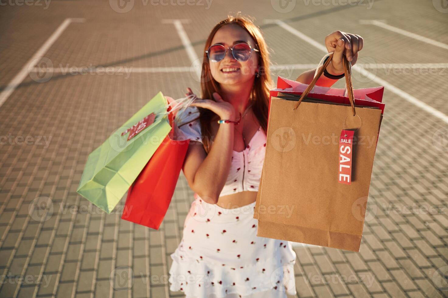 Showing, shopping bag with sale stickers on it. Beautiful woman in casual clothes is outdoors photo