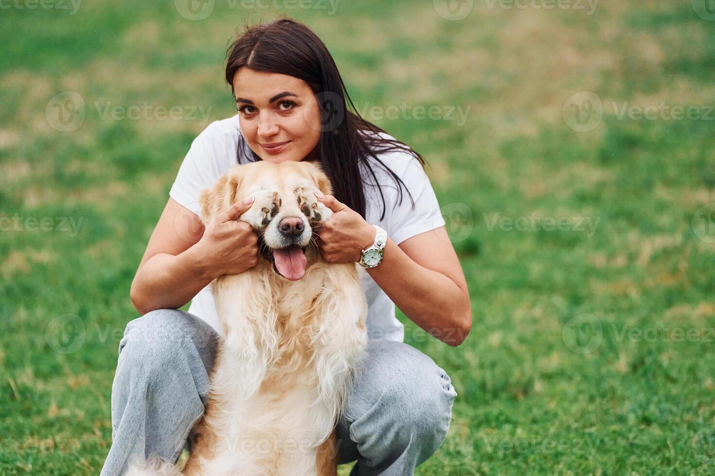 Covering the, eyes with paws. Woman with cute little golden retriever dog is on the green field photo