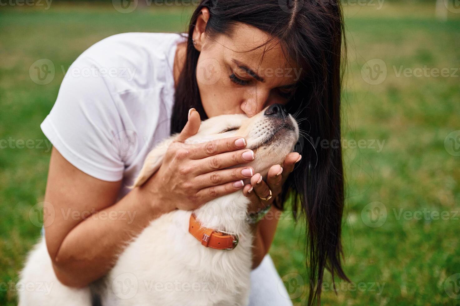 Kissing, the animal. Woman with cute little golden retriever dog is on the green field photo