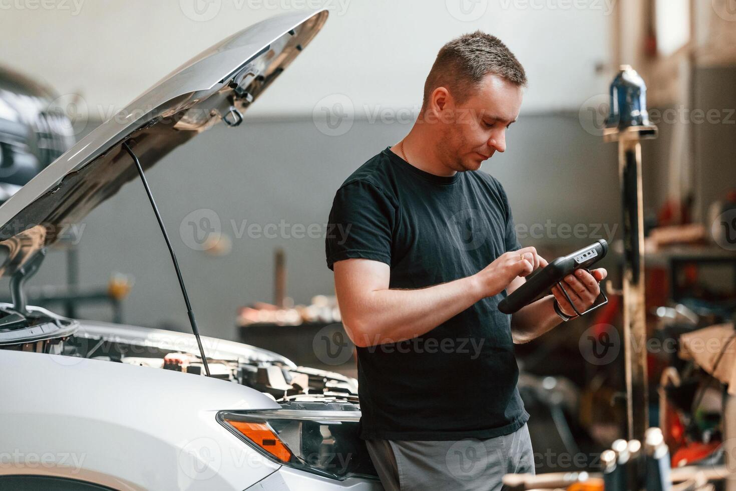 Using the tablet. Man is works in the automobile repairing salon photo