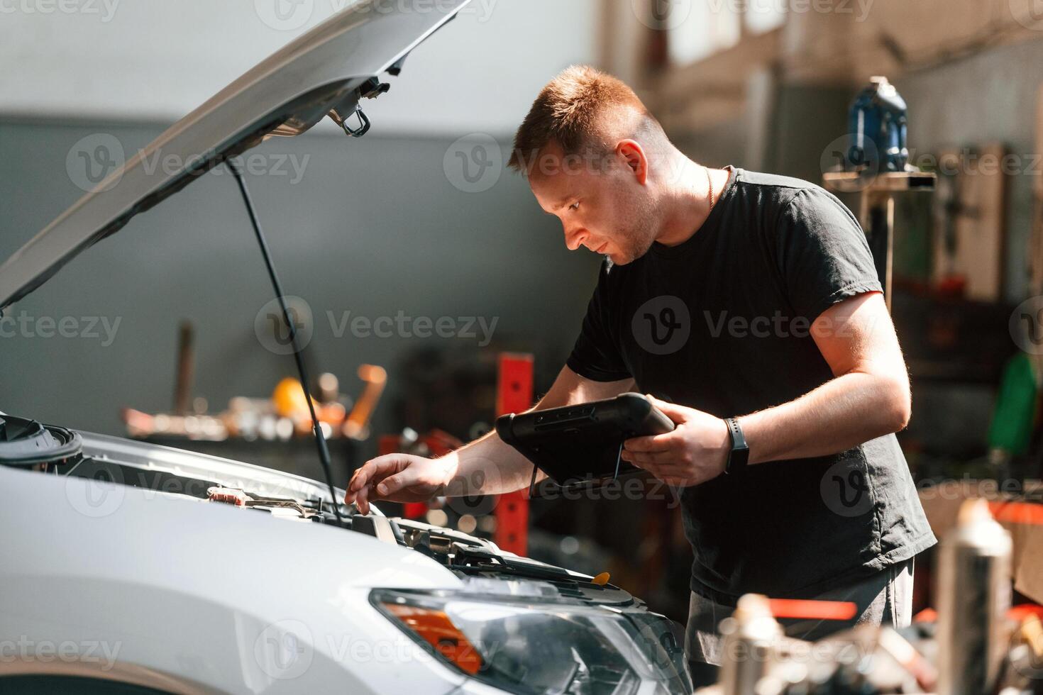 Using the ,tablet. Man is, works in the automobile repairing salon photo