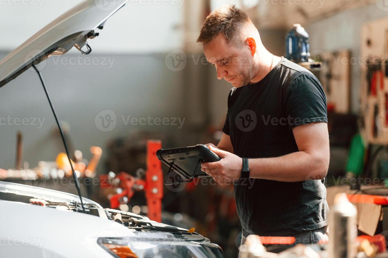 Using ,the tablet.. Man is works in the automobile repairing salon photo