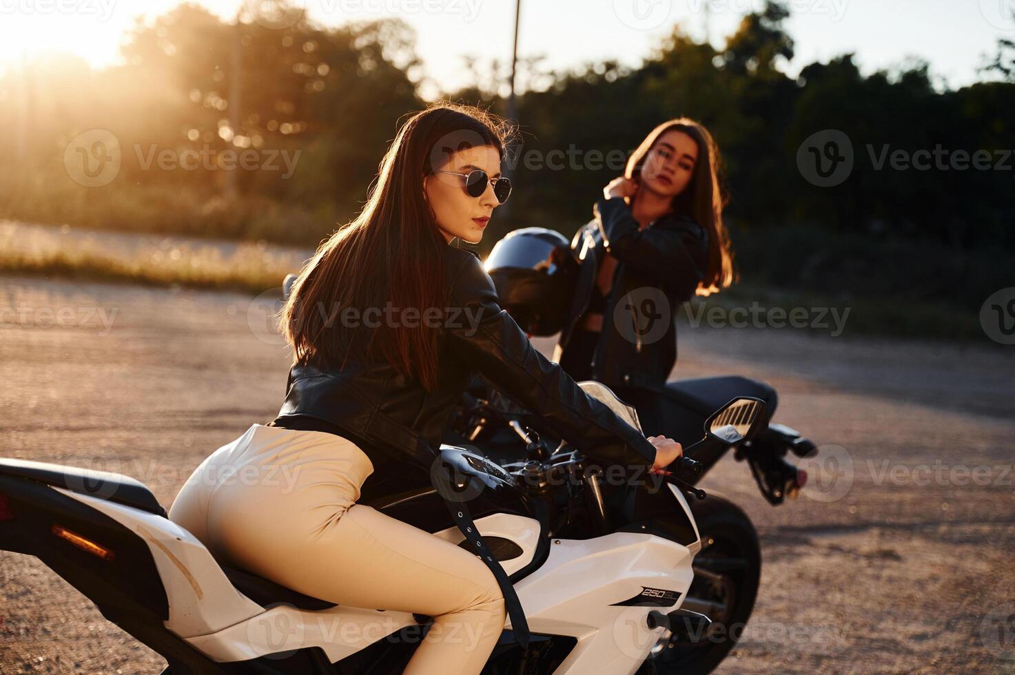 Two women on motorcycles, are, together outdoors photo