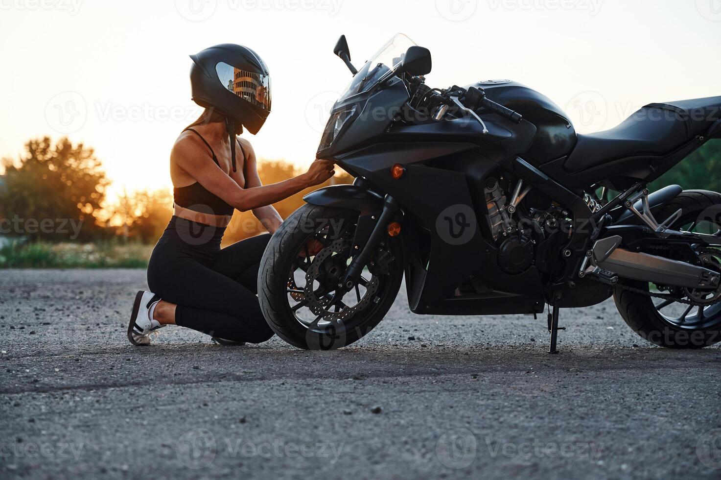 Sitting,, looking at front wheel. Woman is with motorcycle outdoors photo
