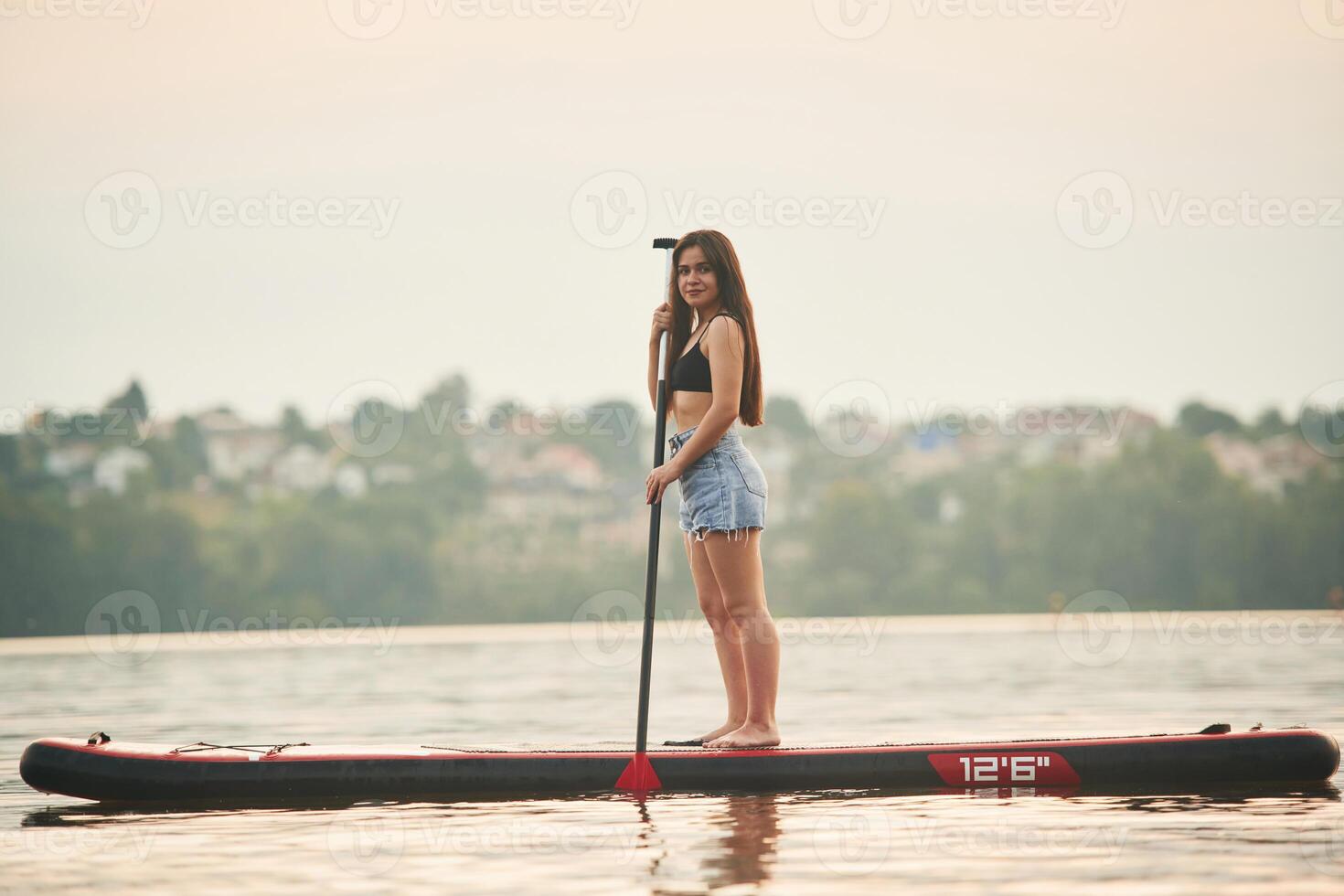 Forest ,and houses on background. Young woman is on sup boards in the lake photo