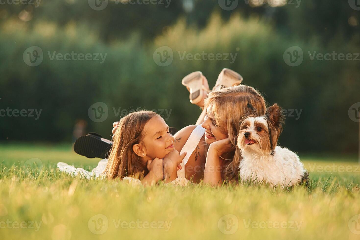 Positive, emotions, on the ,green grass. Mother with her daughter and cute dog are on the field outdoors photo