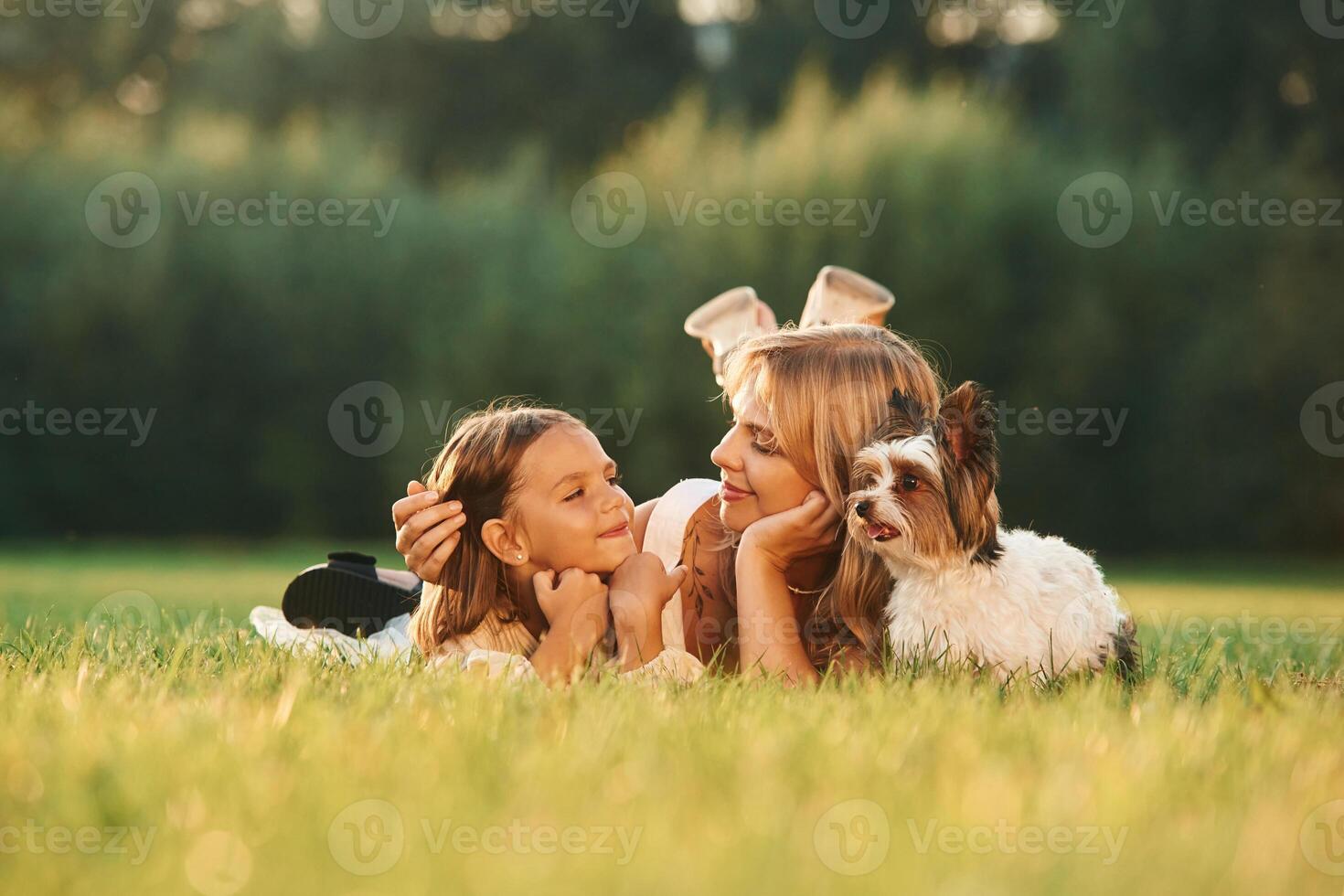 Relaxing,, lying down. Mother with her daughter and cute dog are on the field outdoors photo