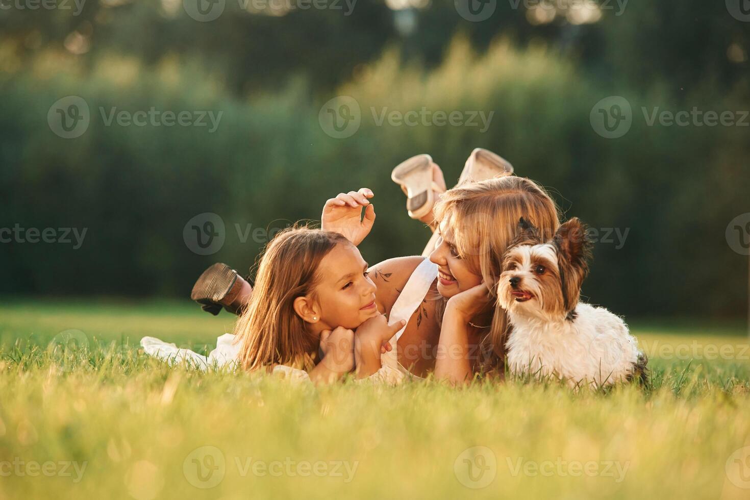 Relaxing, lying, down. Mother with her daughter and cute dog are on the field outdoors photo