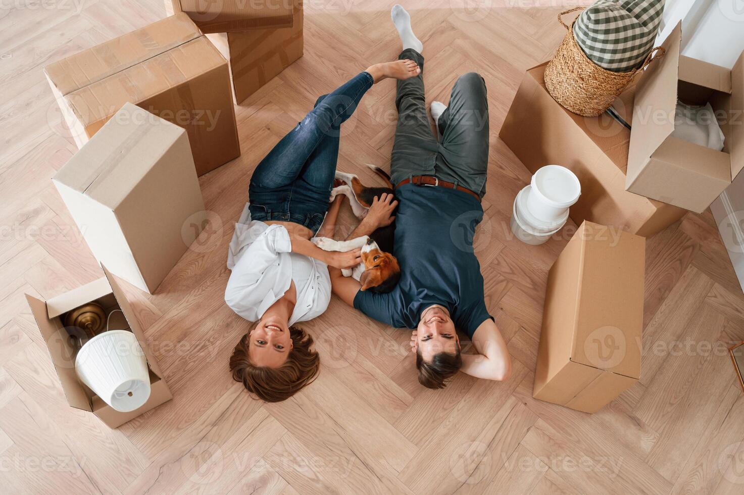 Happy ,young couple ,with dog are moving to new home. Lying down on the floor photo