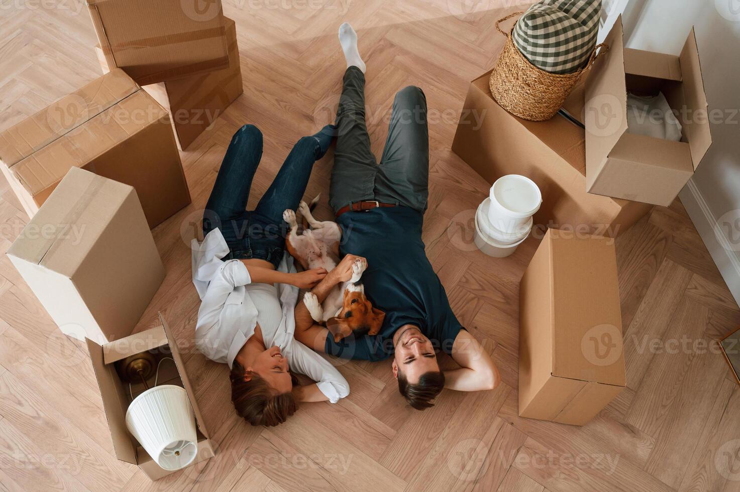 On, the floor, lying down, top view. Young couple with dog are moving to new home photo