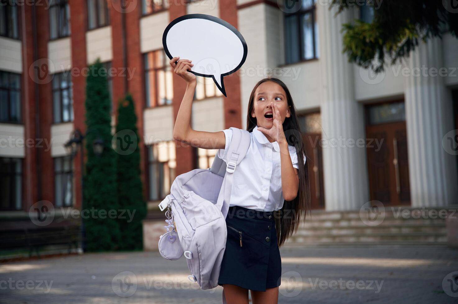 Sticker with thoughts, copy space, for, text. School girl in uniform is outdoors near the building photo