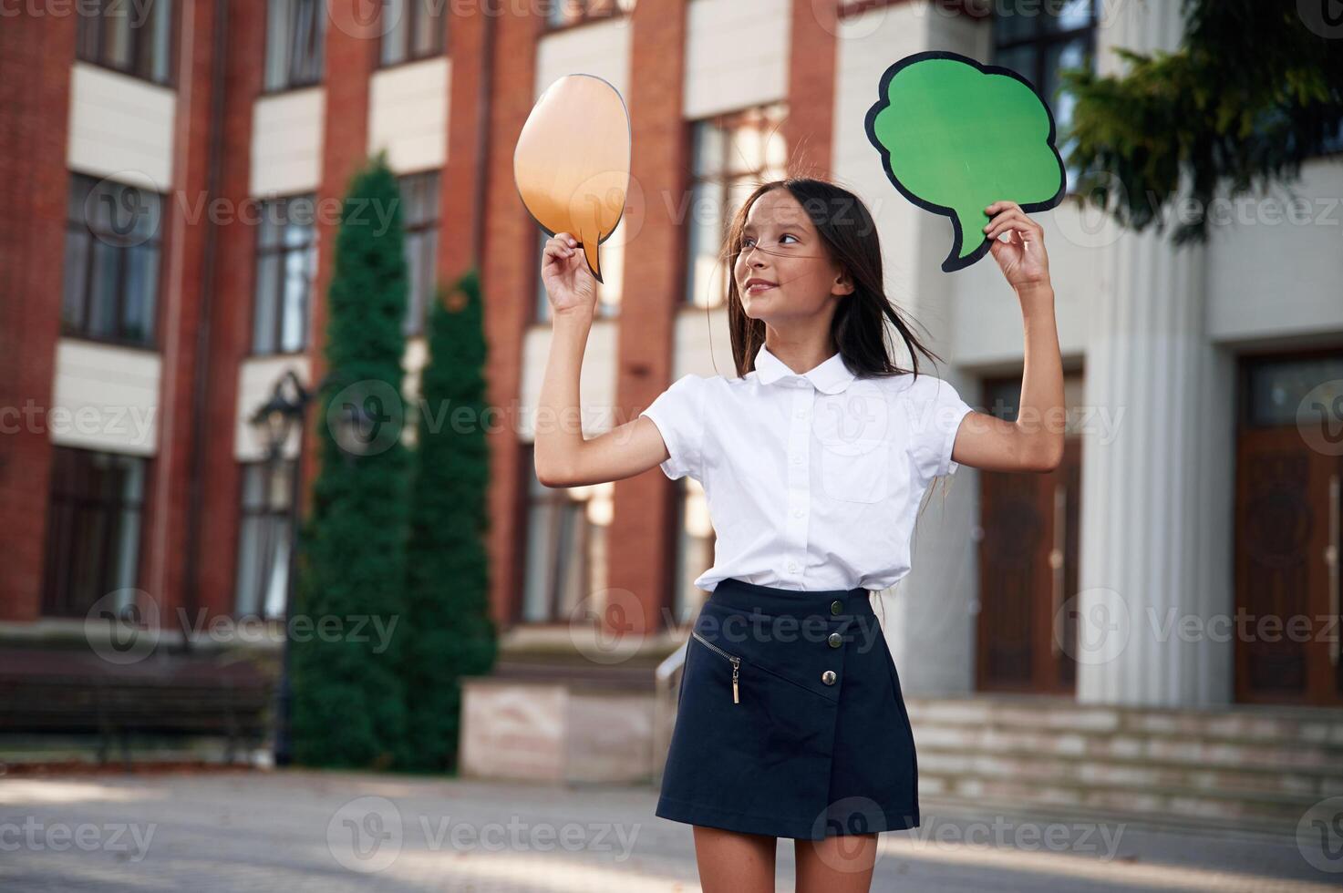 Colorful stickers in hands, copy space ,for, text, thoughts. School girl in uniform is outdoors near the building photo