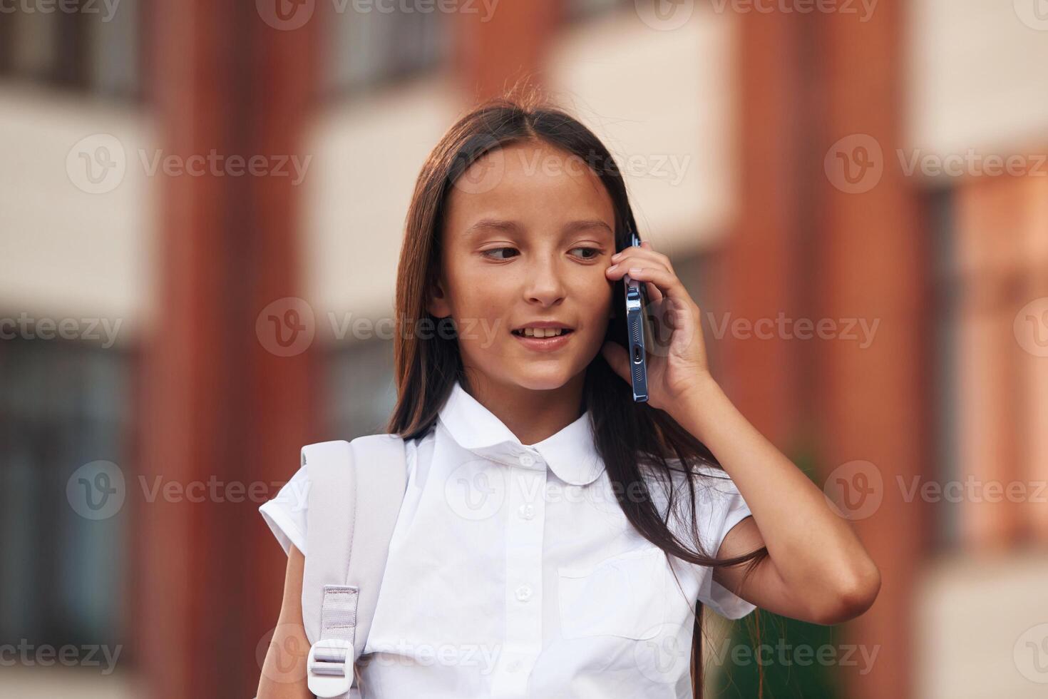 Using ,smartphone. School, girl in uniform is outdoors near the building photo