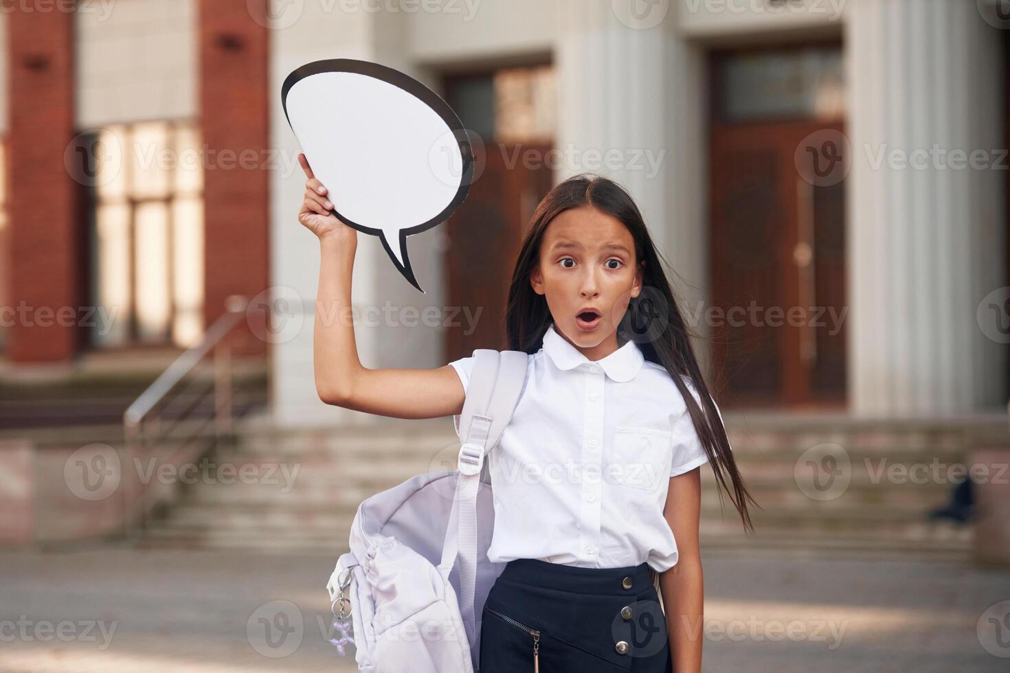 Holding sign ,with ,copy space for text. School girl in uniform is outdoors near the building photo