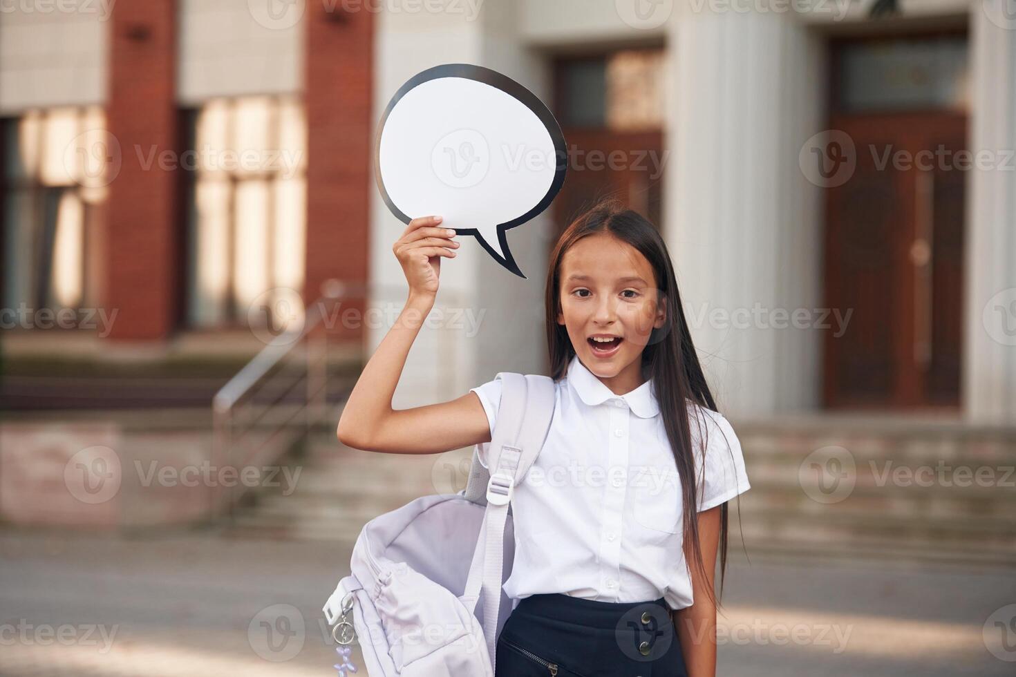 Holding sign ,with, copy space for text. School girl in uniform is outdoors near the building photo