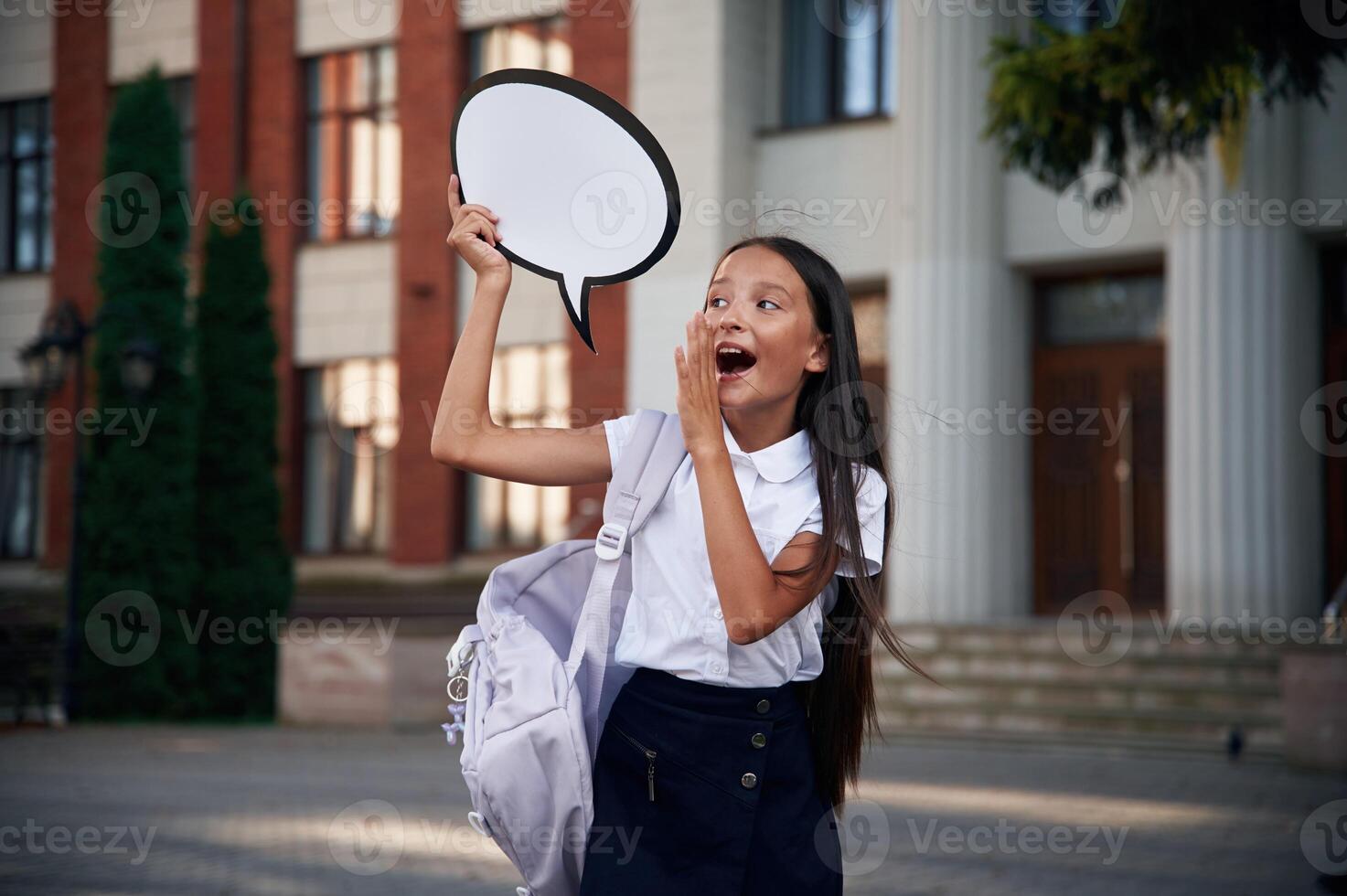 Sticker ,with thoughts, copy space for text. School girl in uniform is outdoors near the building photo