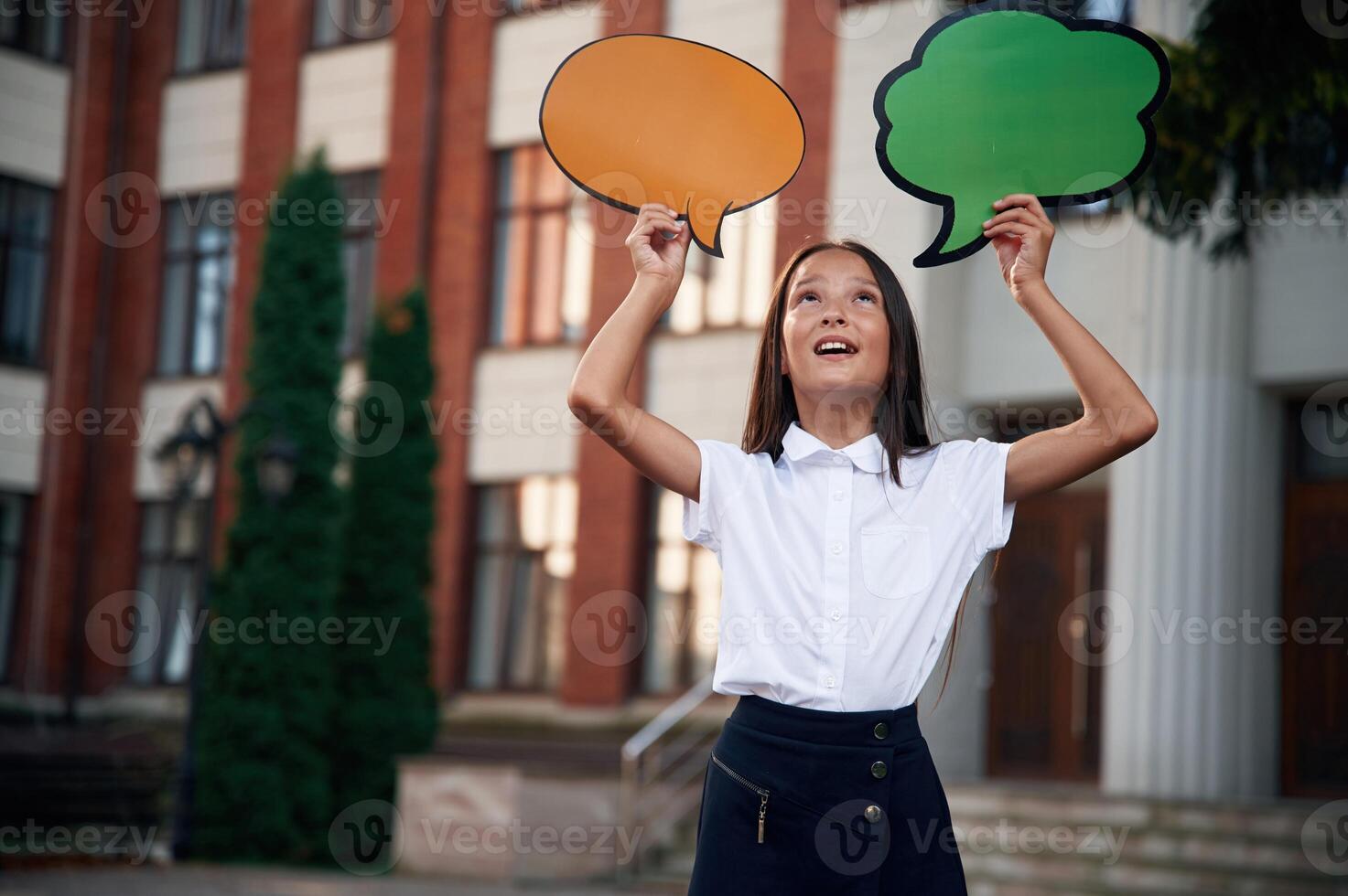 Colorful, stickers in hands, copy space for text, thoughts. School girl in uniform is outdoors near the building photo