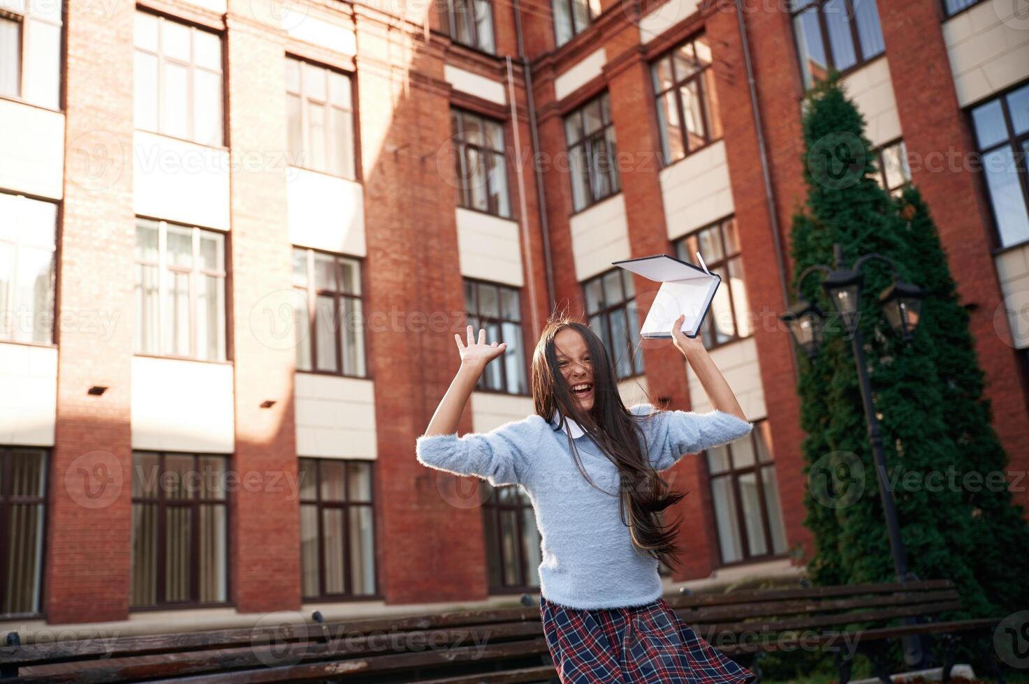 Cheerful, celebrating, success,. School girl in uniform is outdoors near the building photo