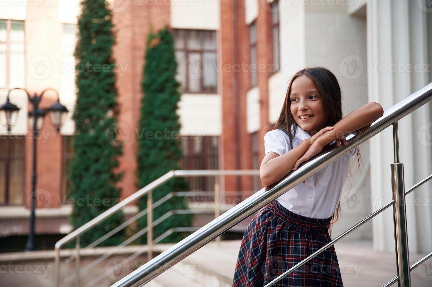 Leaning ,on, the, railing. School girl in uniform is outdoors near the building photo