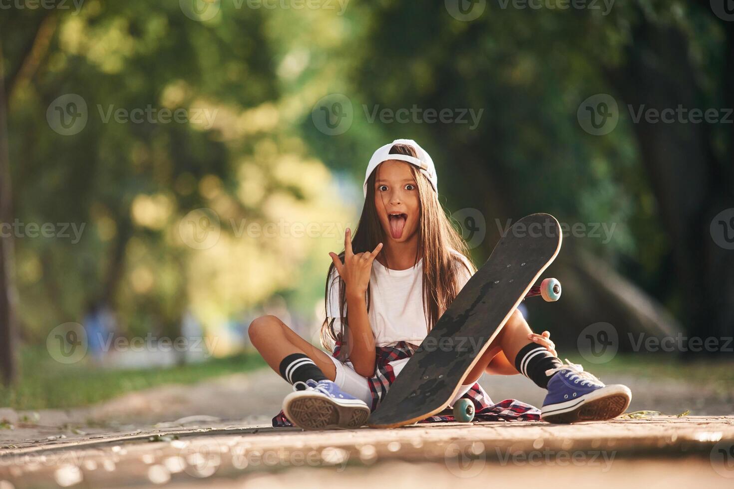Showing metal cool hand gesture. Happy little girl with skateboard outdoors photo