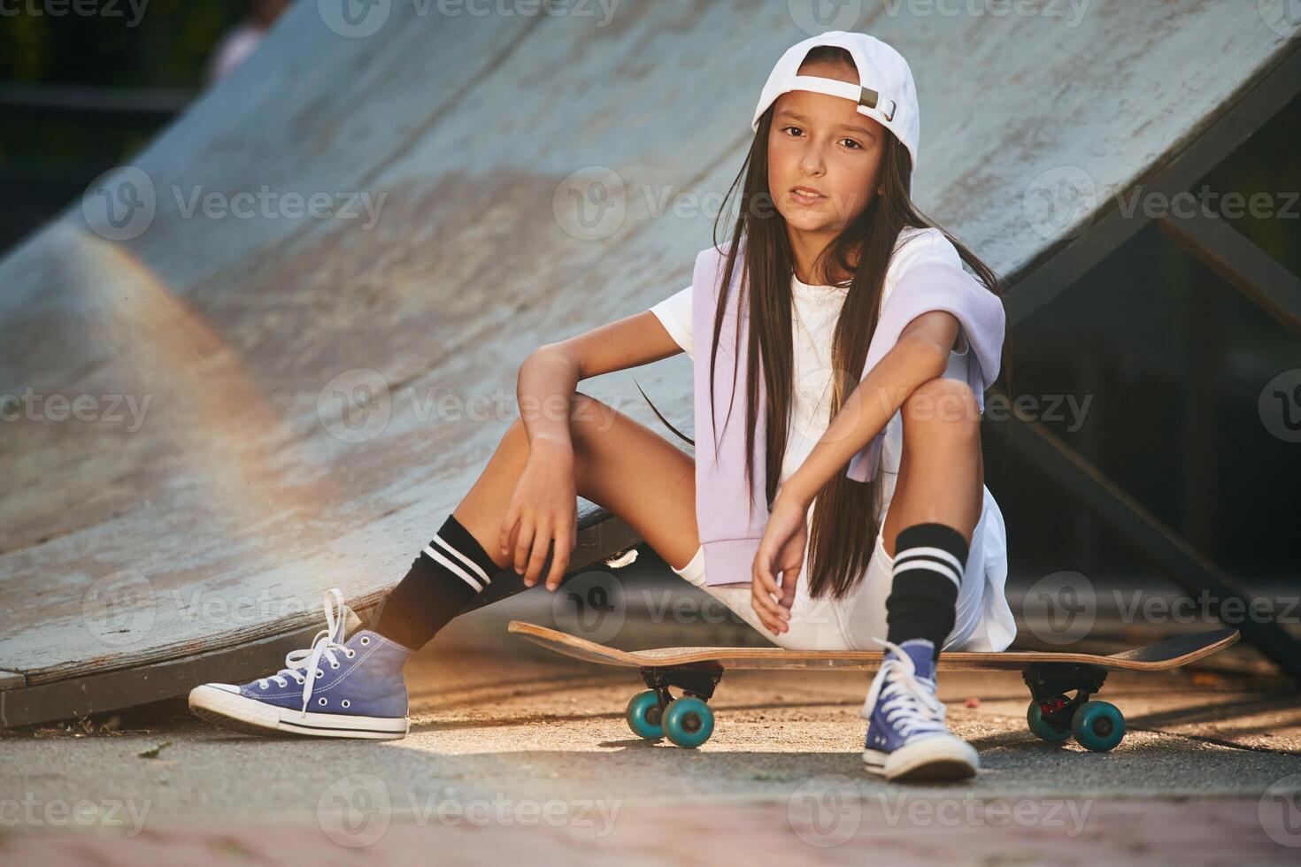 Taking a rest, sitting. Happy, little ,girl with skateboard outdoors photo