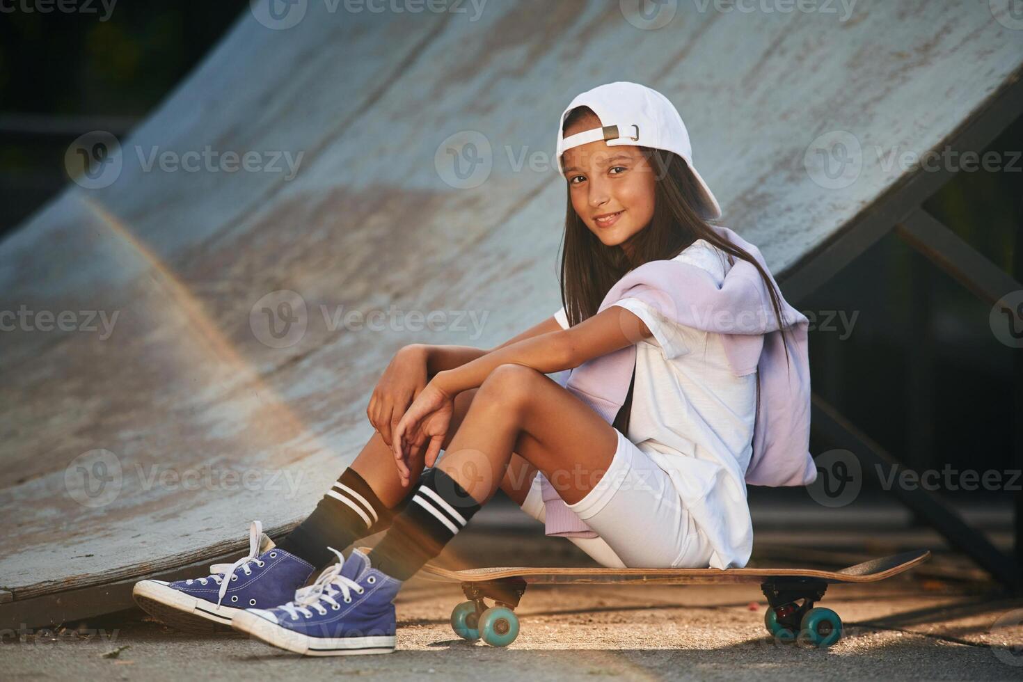 Taking a rest, sitting... Happy little girl with skateboard outdoors photo