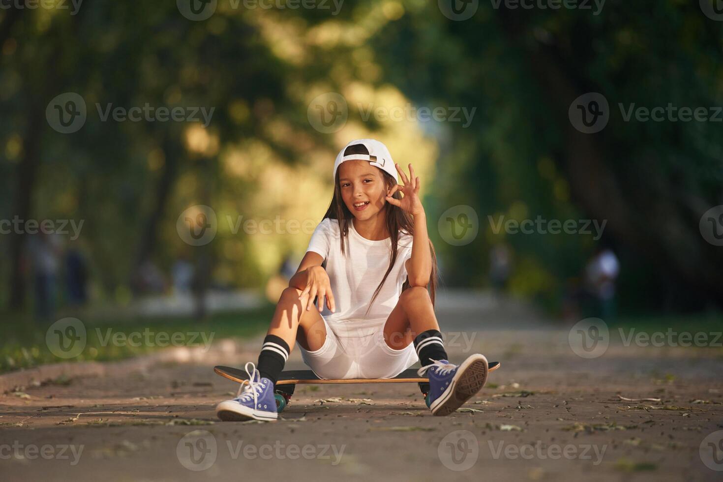 Chilling, sitting and relaxing. Happy, little, girl with skateboard outdoors photo